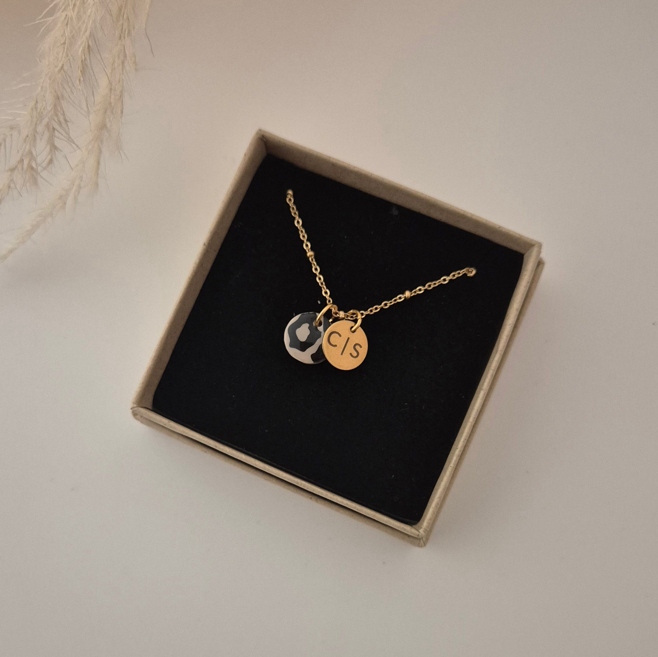 Goldene Kette in der Schmuckschachtel. Leo-Anhänger sowie der goldene Anhänger mit C Trennstrich S graviert zur Größendarstellung.