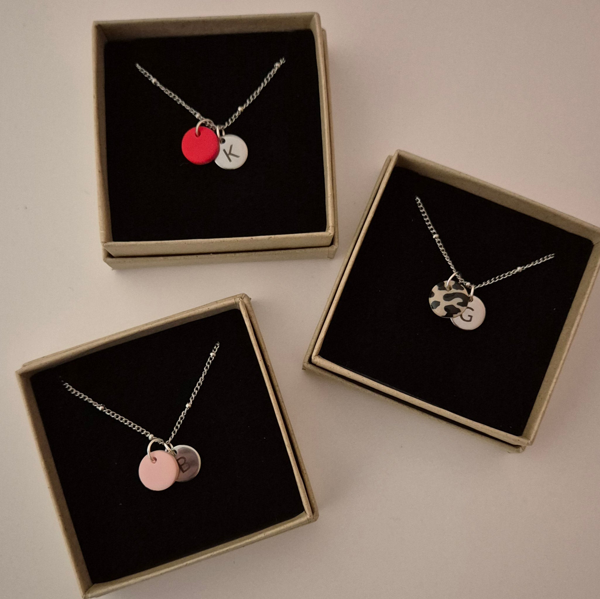 Drei Ketten in silber mit der gleichen Punkt-Struktur wie die goldene Kette. Die Ketten liegen in jeweils einer Schmuckschachtel und haben jeweils einen anderen Anhänger in rot, rosa und Leo. Jede Kette hat außerdem einen silbernen Anhänger mit Gravur in den gleichen Größen wie die goldene Kette.