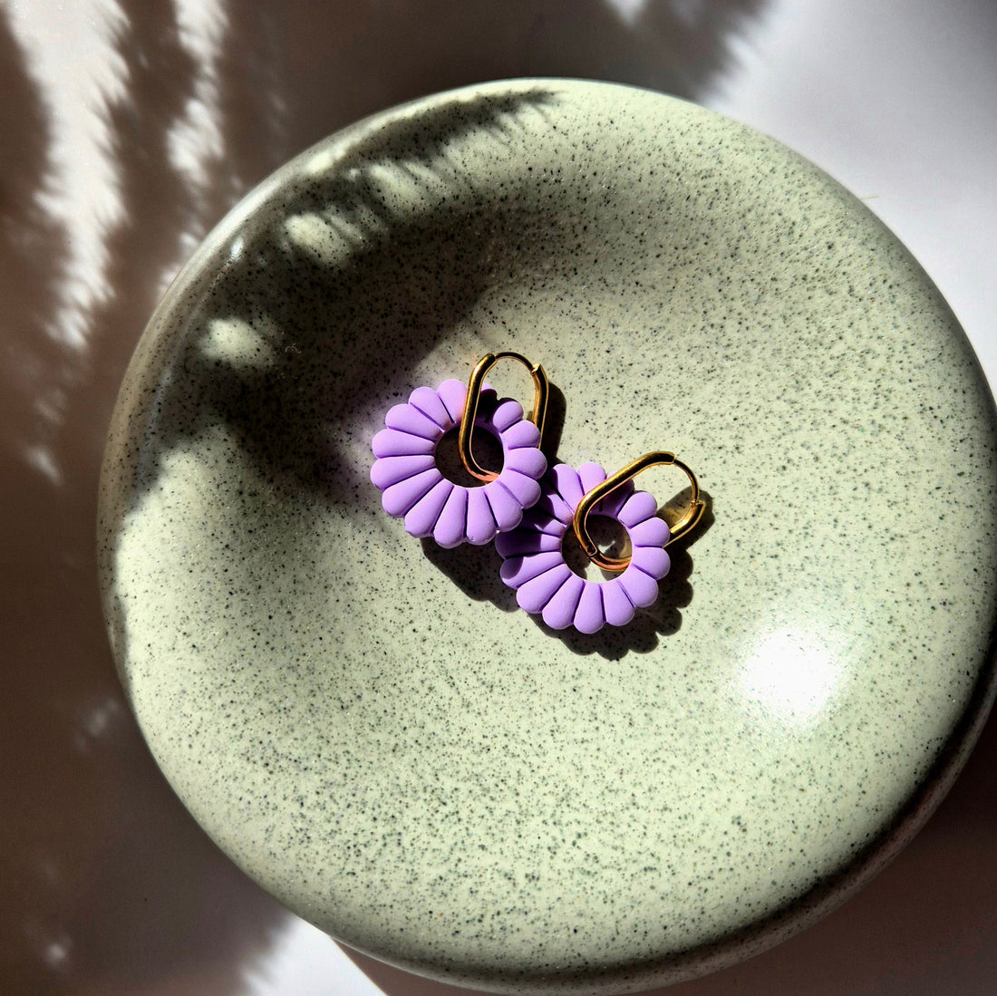 Lilia Ohrringe in flieder auf einer goldenen, rechteckigen aber abgerundeten Creole gefädelt.