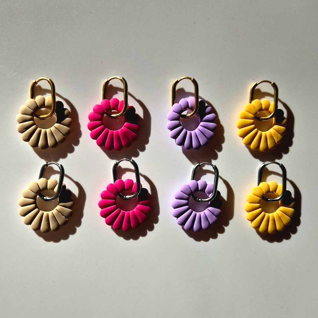 Lilia Ohrringe mit filigranem Design in beige, pink, sonnengelb und lila – Die Ohrringe bestehen aus einem Kreis mit Lamellen und sind auf eine goldene oder silberne rechteckige, aber abgerundete Creole gefädelt.