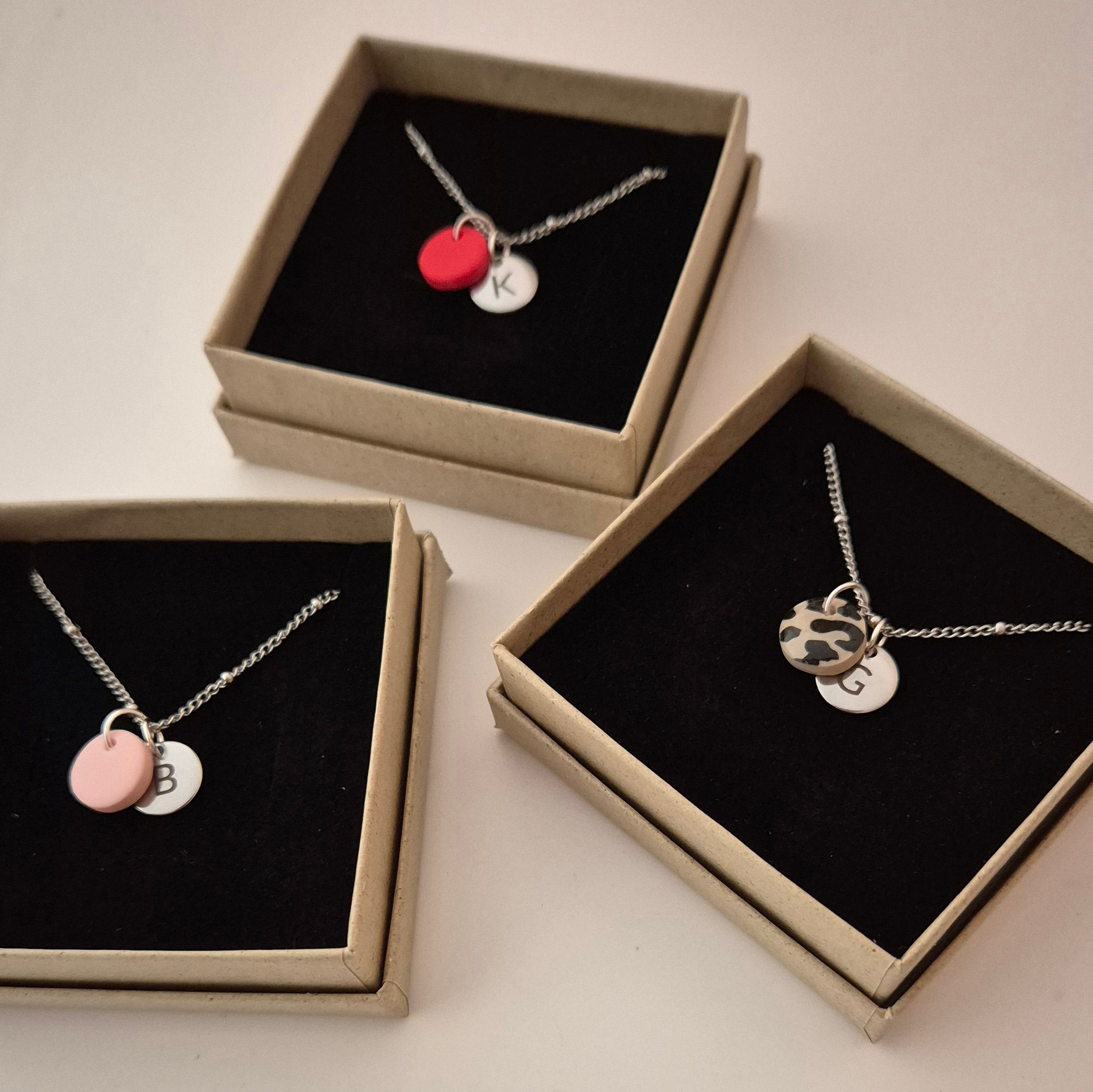 Drei Ketten in silber mit der gleichen Punkt-Struktur wie die goldene Kette. Die Ketten liegen in jeweils einer Schmuckschachtel und haben jeweils einen anderen Anhänger in rot, rosa und Leo. Jede Kette hat außerdem einen silbernen Anhänger mit Gravur in den gleichen Größen wie die goldene Kette.